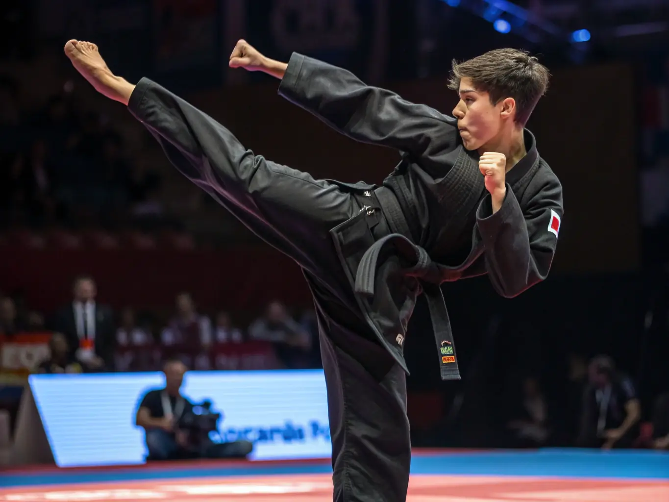 A teenager in a blue taekwondo uniform executing a spinning kick during a sparring session, showcasing agility and technique.